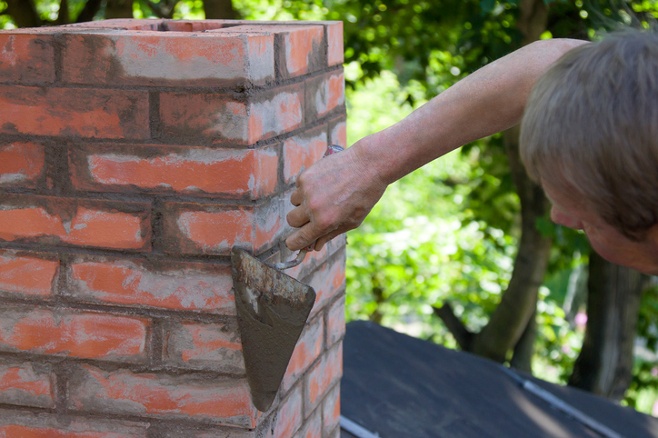 A man working with a trowel and making a chimney of red bricks in summer