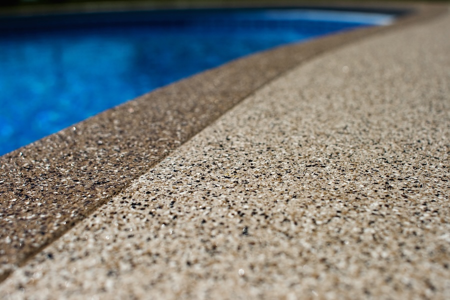 A closeup of a decorative concrete overlay, next to a blue swimming pool.